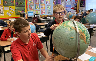 Two boys look at a globe while studying geography.